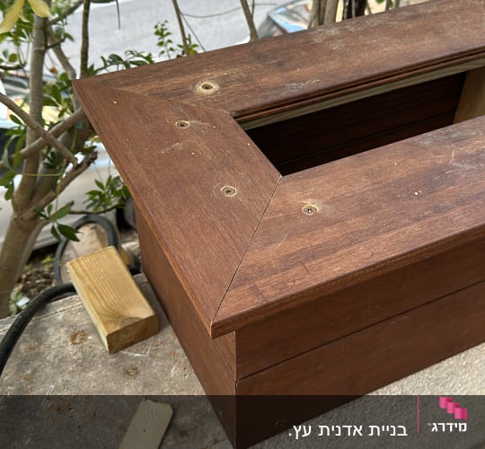 קופסת עץ עם ברגים על קיר בטון בגינה